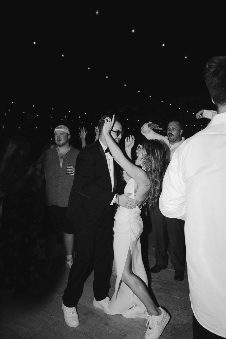 Black and white photo of newlyweds dancing under string lights