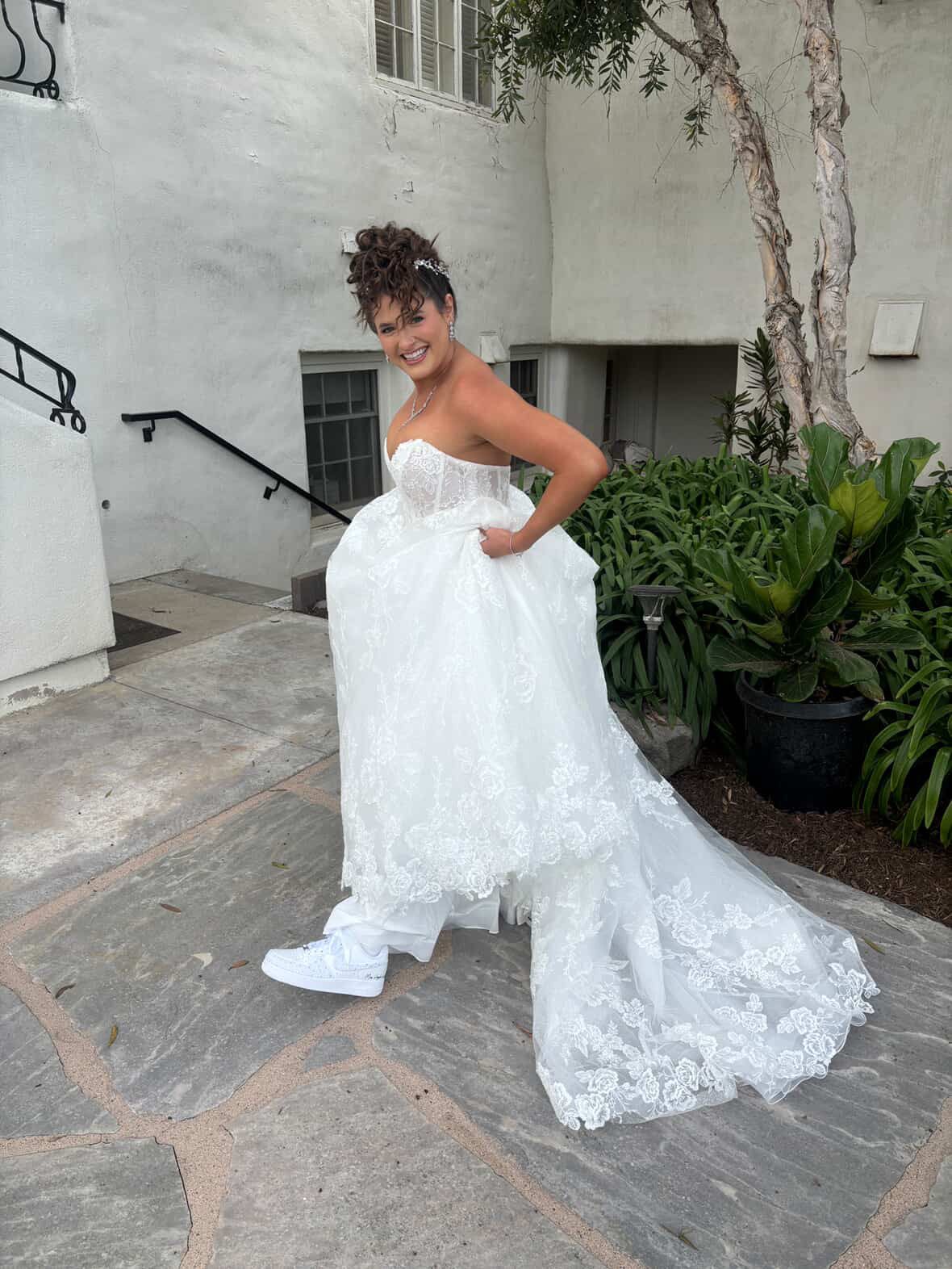 Bride smiling in long lace gown wearing white custom wedding sneakers
