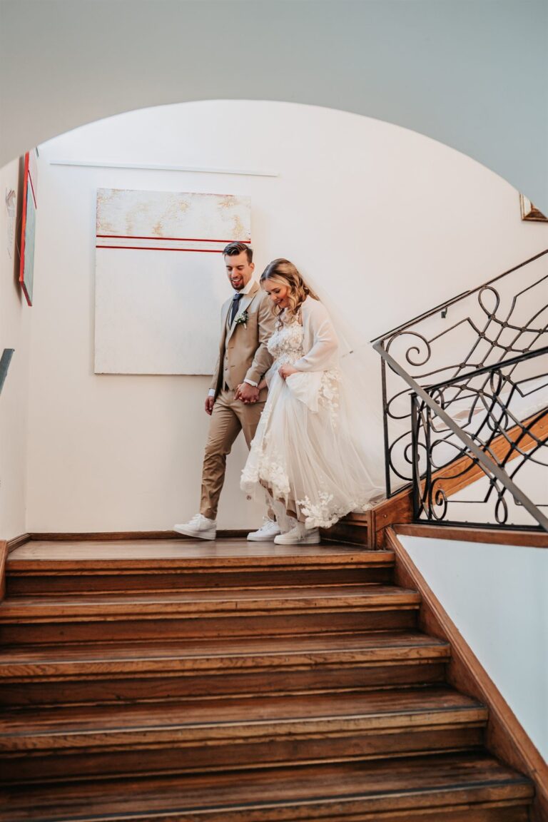 Newlywed couple walking hand in hand down a staircase in custom sneakers