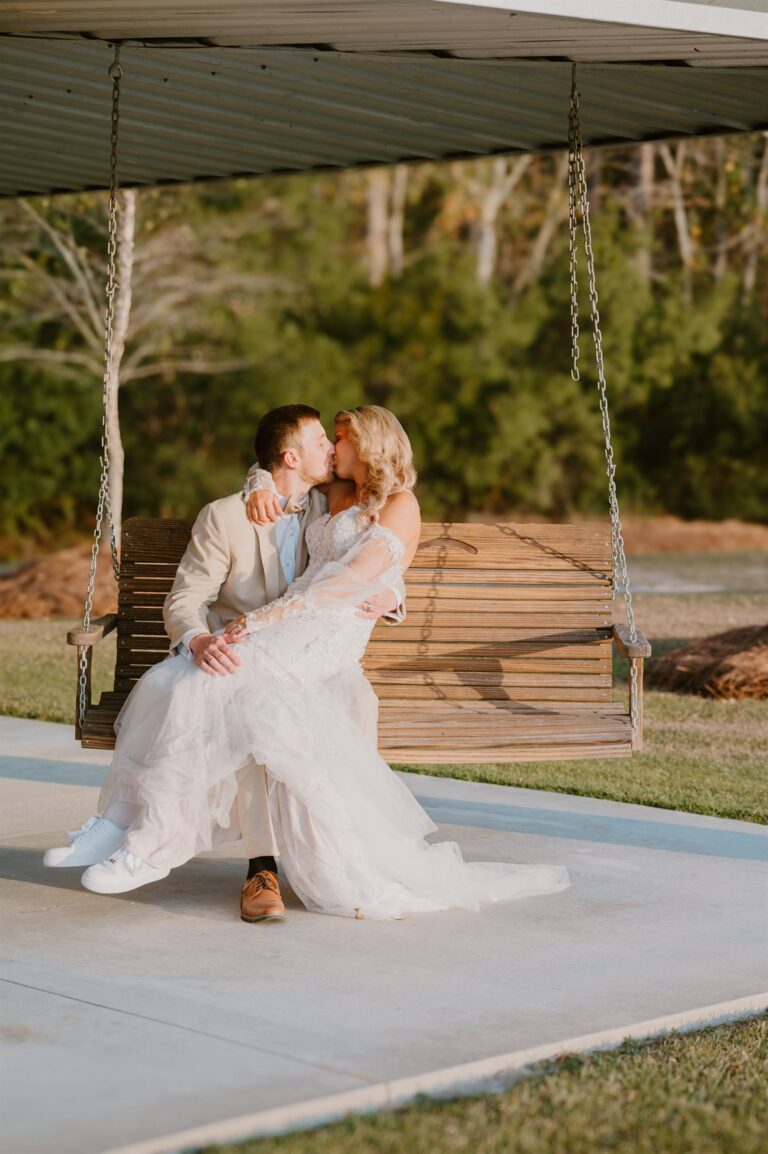 Bride and groom kissing on a porch swing in their wedding sneakers